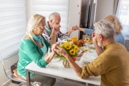 Téléchargez les photos : Groupe de personnes âgées célébrant Thanksgiving ensemble à la maison lors d'un dîner traditionnel, priant et exprimant leur gratitude avant le dîner - en image libre de droit