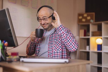 Téléchargez les photos : Homme portant un casque et assis à son bureau à la maison, ayant une conférence téléphonique tout en travaillant à distance de la maison - en image libre de droit