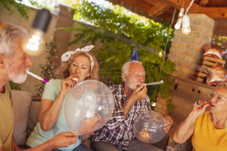 Photo for Senior people having fun at birthday party, blowing party whistles and waving with balloons - Royalty Free Image