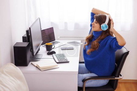 Téléchargez les photos : Jeune femme travaillant au bureau à la maison s'étirant tandis qu'elle était assise à son bureau - en image libre de droit