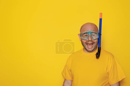 Téléchargez les photos : Mi-trentaine homme chauve en surpoids s'amusant à porter un masque de plongée et à faire des visages sur fond jaune avec espace de copie vacances d'été, tourisme et concept de voyage - en image libre de droit