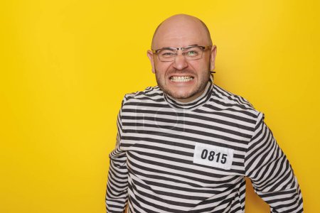 Photo for Man wearing prison uniform costume having fun making faces on yellow colored background with copy space - Royalty Free Image