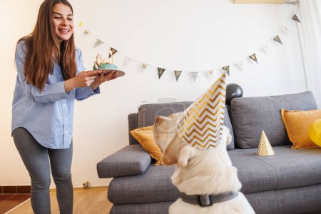 Foto de Mujer teniendo una fiesta de cumpleaños para su perro mascota, trayéndole un pastel de cumpleaños sorpresa - Imagen libre de derechos