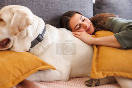 Téléchargez les photos : Femme relaxante à la maison faisant une sieste l'après-midi allongée sur le canapé dormant et embrassant son chien de compagnie - en image libre de droit