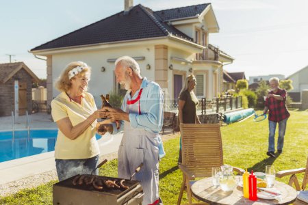 Photo for Group of cheerful active senior people having a backyard barbecue party, grilling meat and vegetables and having fun playing badminton - Royalty Free Image