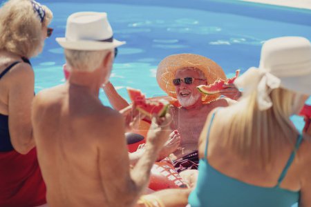 Photo for Group of cheerful senior people sitting at the edge of a swimming pool eating watermelon, sunbathing and having fun outdoors on a hot summer day - Royalty Free Image