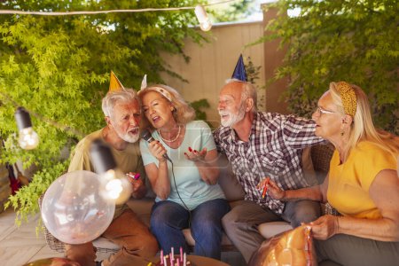 Photo for Group of cheerful senior people having a birthday party for a friend, having fun singing karaoke - Royalty Free Image