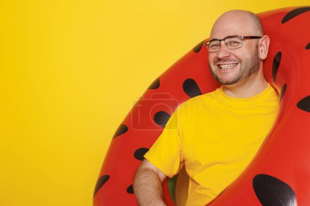 Téléchargez les photos : Joyeux homme tenant anneau de natation de pastèque gonflable sur fond jaune avec espace de copie - vacances d'été et concept de voyage - en image libre de droit