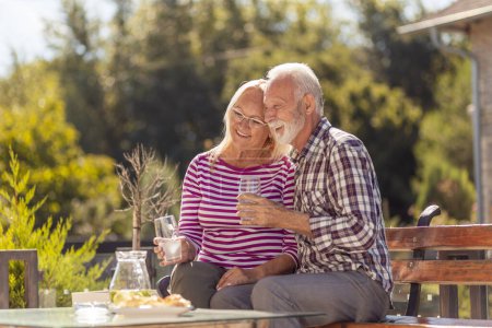Photo for Happy senior couple enjoying their time together having breakfast in the backyard of their home, drinking lemonade and relaxing outdoors - Royalty Free Image