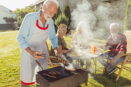 Photo for Senior neighbors having fun spending sunny summer day together outdoors, grilling meat and relaxing - Royalty Free Image