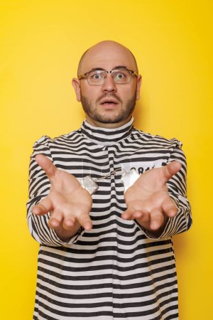Photo for Man wearing prison uniform costume and handcuffs having fun making faces on yellow colored background - Royalty Free Image