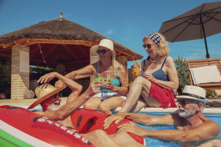 Photo for Two senior couples sunbathing, relaxing and having fun at the swimming pool on a hot sunny summer day, enjoying their vacation, drinking cocktails and cooling down in the pool - Royalty Free Image