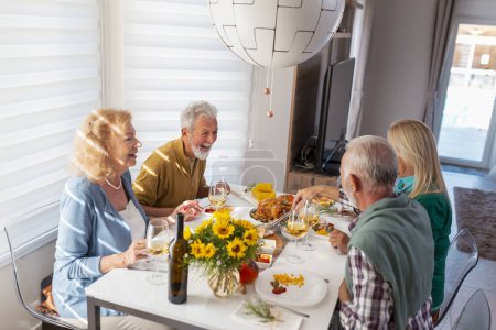 Foto de Grupo de personas mayores divirtiéndose mientras celebran Acción de Gracias juntos en casa durante la cena tradicional - Imagen libre de derechos