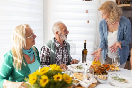 Foto de Grupo de amigos mayores divirtiéndose mientras celebran Acción de Gracias juntos en casa durante la cena tradicional - Imagen libre de derechos