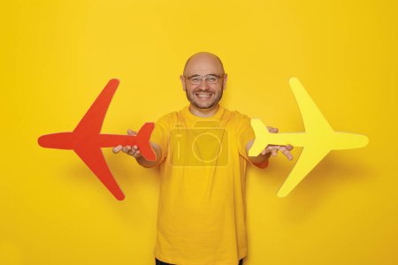 Téléchargez les photos : Portrait d'un homme tenant des avions en carton sur fond jaune - concept de voyage aérien et de vacances d'été - en image libre de droit