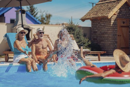 Foto de Grupo de personas mayores que se divierten pasando el día soleado caliente del verano en la piscina, tomando el sol y salpicando el agua entre sí, enfriándose y relajándose mientras que en vacaciones - Imagen libre de derechos
