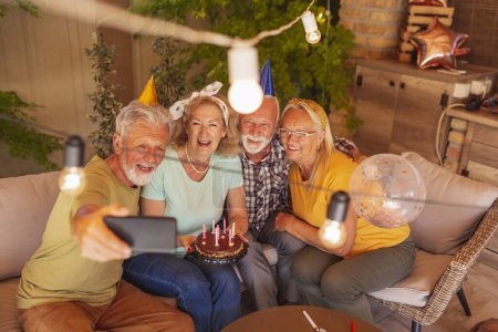 Photo for Group of cheerful senior people having fun celebrating friend's birthday, taking a selfie with birthday cake while at the party - Royalty Free Image