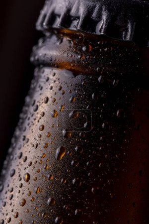 Téléchargez les photos : Détail de la bouteille de bière froide et humide avec des gouttelettes d'eau de rosée et de condensat à la surface du verre - en image libre de droit