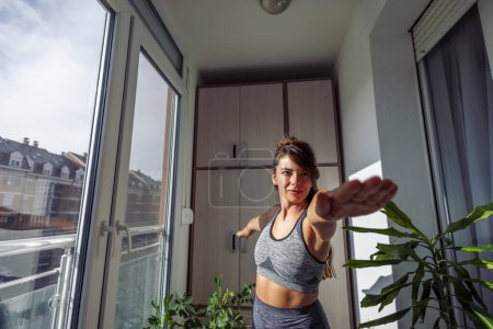 Téléchargez les photos : Jeune femme en vêtements de sport faisant de l'exercice à la maison le matin, faisant du yoga - en image libre de droit