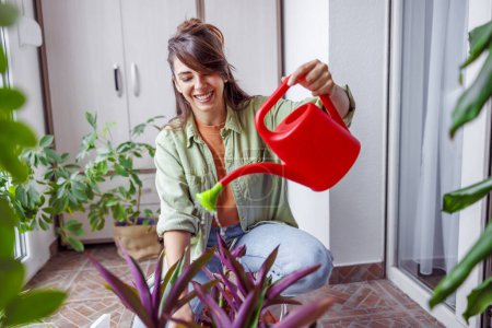 Photo for Beautiful young woman enjoying leisure time at home, relaxing while watering houseplants - Royalty Free Image