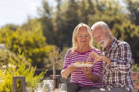Photo for Happy senior couple enjoying their time together having an outdoor brunch in the backyard of their home - Royalty Free Image
