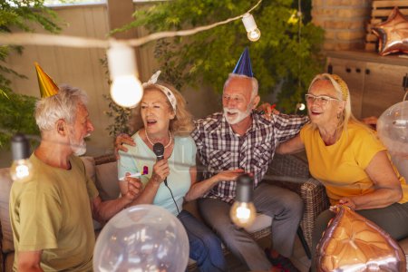 Foto de Grupo de alegres amigos mayores divirtiéndose en una fiesta de cumpleaños cantando karaoke - Imagen libre de derechos