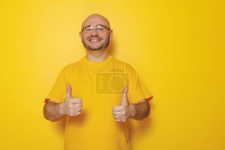 Photo for Portrait of mid 30s bald man wearing glasses showing thumbs up on yellow color background with copy space - Royalty Free Image