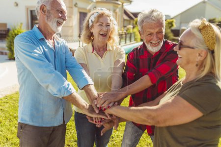 Photo for Group of cheerful active senior people having fun playing football on the lawn in the backyard, gathered in circle, holding hands all together in the middle before the match - Royalty Free Image