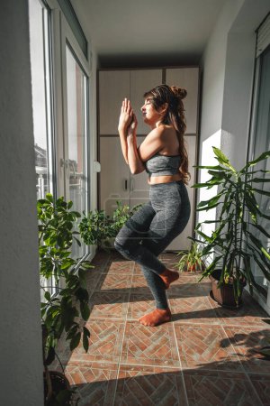 Junge Frau in Sportkleidung, die morgens zu Hause Yoga macht, in Adler-Pose