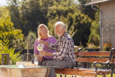 Foto de Pareja mayor disfrutando de su tiempo juntos desayunando en el patio trasero de su casa, bebiendo limonada y relajándose al aire libre - Imagen libre de derechos