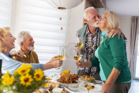 Foto de Dos parejas mayores se reunieron para la cena de Acción de Gracias, anfitrión expresando gratitud a su esposa por hacer una comida encantadora y hacer un brindis levantando copas de vino, dando la bienvenida a los invitados - Imagen libre de derechos