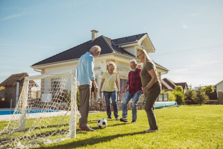 Photo for Active senior friends having fun playing football on the lawn in the backyard by the swimming pool, enjoying sunny summer day outdoors - Royalty Free Image