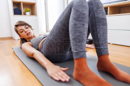 Foto de Mujer joven activa en ropa deportiva haciendo crujidos laterales mientras hace ejercicio en casa; mujer haciendo entrenamiento en casa en línea - Imagen libre de derechos