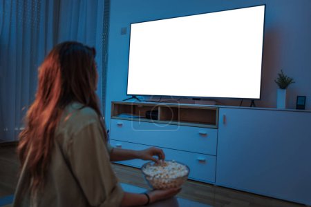 Téléchargez les photos : Jeune femme jouissant de loisirs à la maison la nuit, regarder un film à la télévision et manger du pop-corn - en image libre de droit