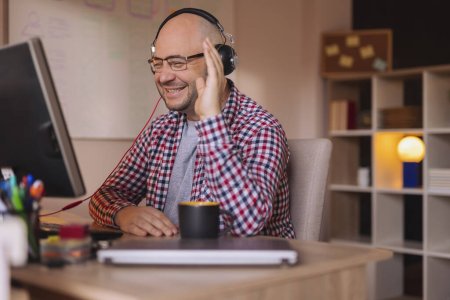 Foto de Hombre con auriculares y sentado en su escritorio en la oficina en casa, teniendo una llamada de conferencia mientras trabaja desde casa - Imagen libre de derechos