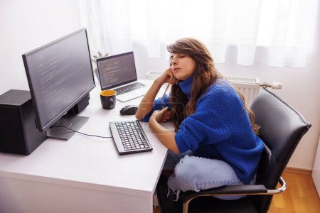 Foto de Desarrollador de software femenino sentado en su escritorio en la oficina en casa tomando una siesta de energía mientras trabaja remotamente desde casa, cansado mientras trabaja horas extras - Imagen libre de derechos