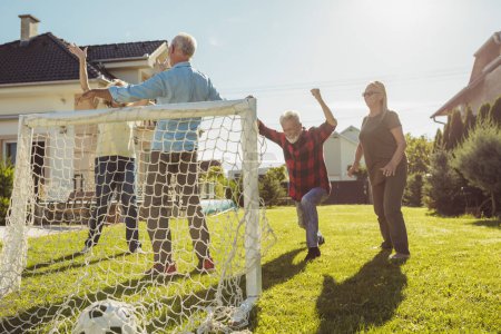 Photo for Group of active senior people having fun playing football on the lawn in the backyard, enjoying sunny summer day outdoors, celebrating after scoring a goal - Royalty Free Image
