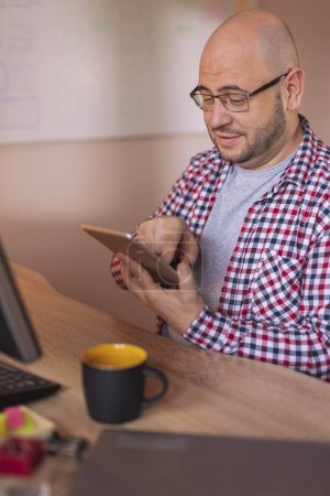 Téléchargez les photos : Designer UX assis à son bureau dans un bureau, en utilisant un ordinateur tablette tout en travaillant sur un nouveau projet - en image libre de droit