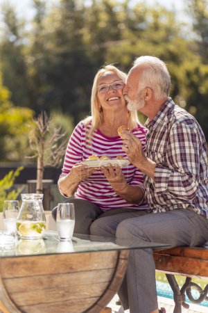 Foto de Feliz pareja de ancianos disfrutando de su tiempo juntos desayunando al aire libre en el patio trasero de su casa - Imagen libre de derechos