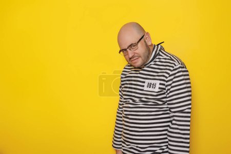 Téléchargez les photos : Homme portant un costume uniforme de prison s'amusant à faire des visages sur fond jaune avec espace de copie - en image libre de droit