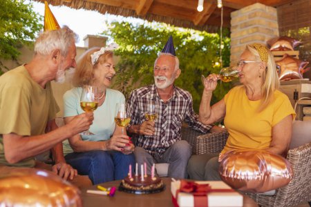 Foto de Grupo de amigos mayores alegres activos que usan sombreros de fiesta que se divierten celebrando cumpleaños, haciendo un brindis y bebiendo vino - Imagen libre de derechos