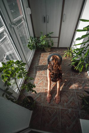 Foto de Vista de ángulo alto de la hermosa mujer joven en ropa deportiva haciendo ejercicio en casa, relajándose mientras hace yoga por la mañana - Imagen libre de derechos