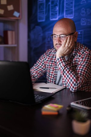 Téléchargez les photos : Homme assis à son bureau, utilisant un ordinateur portable tout en travaillant tard dans le bureau à la maison - en image libre de droit