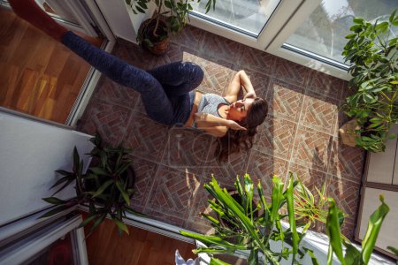 Téléchargez les photos : Vue du dessus de la jeune femme en forme faisant des redressements assis tout en travaillant à la maison le matin - en image libre de droit