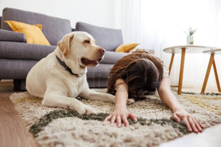 Téléchargez les photos : Jeune femme active en vêtements de sport faisant du yoga à la maison avec son chien de compagnie à ses côtés - en image libre de droit