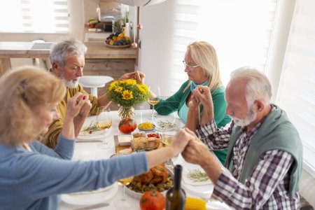 Foto de Grupo de personas mayores que celebran el Día de Acción de Gracias juntos en casa durante la cena tradicional, orando y expresando gratitud antes de la cena - Imagen libre de derechos