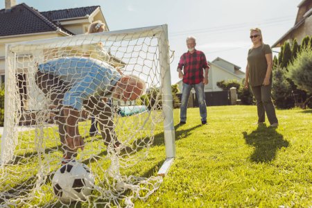 Foto de Amigos mayores activos que se divierten jugando al fútbol en el césped en el patio trasero, disfrutando del soleado día de verano al aire libre - Imagen libre de derechos