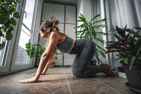 Téléchargez les photos : Belle jeune femme en vêtements de sport faire de l'entraînement à la maison, se détendre tout en faisant du yoga le matin - en image libre de droit