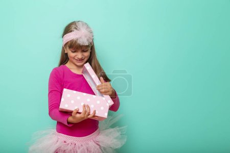 Téléchargez les photos : Belle petite fille célébrant son anniversaire, ouvrant un cadeau, isolé sur fond de couleur menthe - en image libre de droit