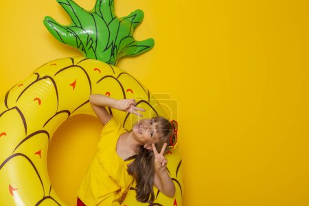 Photo for Little girl sitting in an inflatable pineapple shaped swim ring, getting ready for beach summer vacation, isolated on yellow colored background - Royalty Free Image